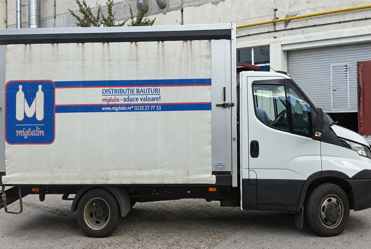 Autoutilitară albă Migdalin cu logo-ul cu sticle și „Distribuție băuturi, migdalin, aduce valoare!" pe bena