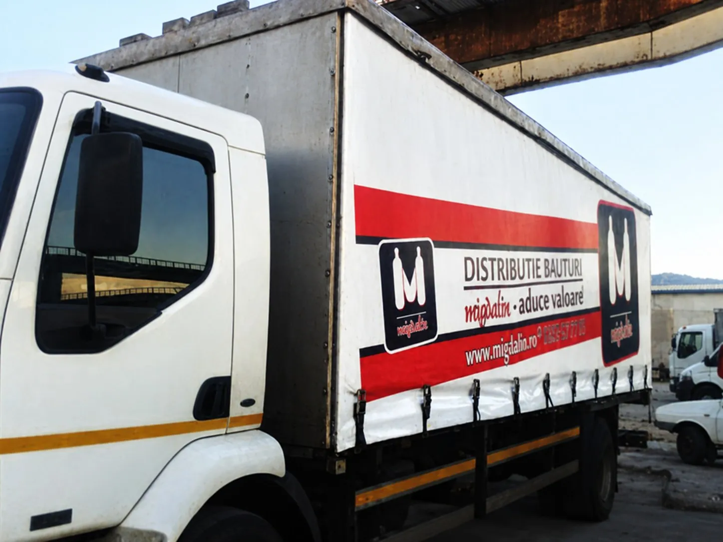 Camion de marfă Migdalin cu logo-ul cu sticle și sloganul „aduce valoare" pe prelată