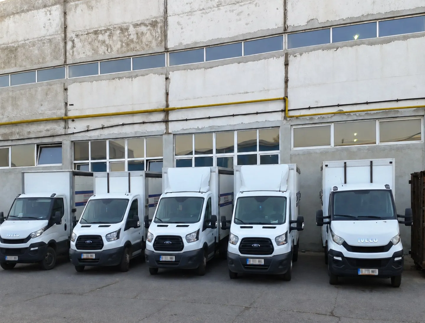 Cinci autoutilitare albe Migdalin parcate una lângă alta în fața depozitului