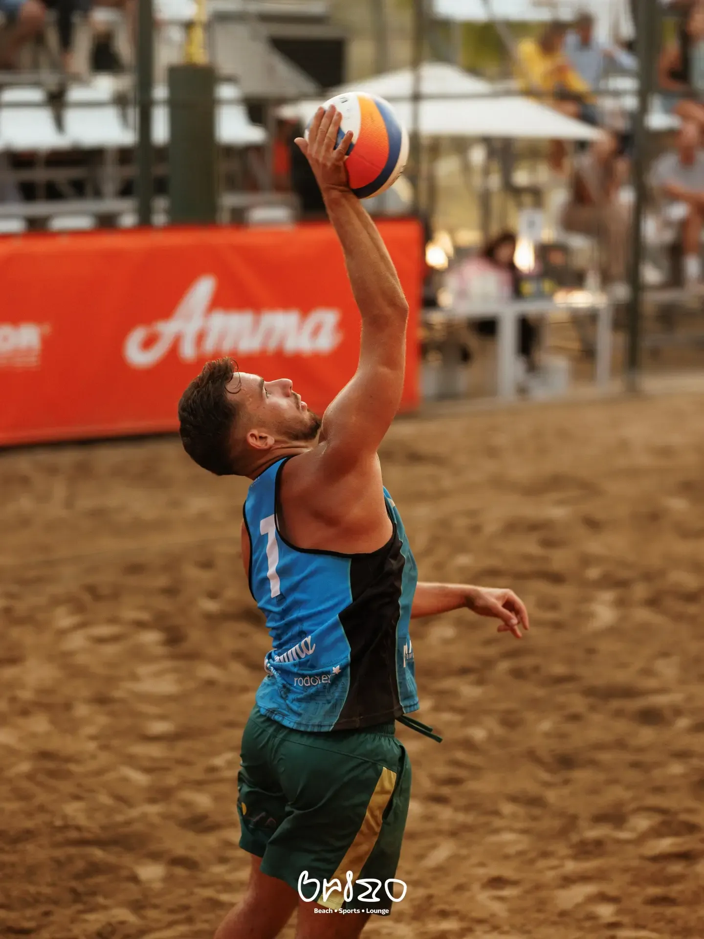 Jucător de volei pe plajă servind, cu bannerul Amma în fundal