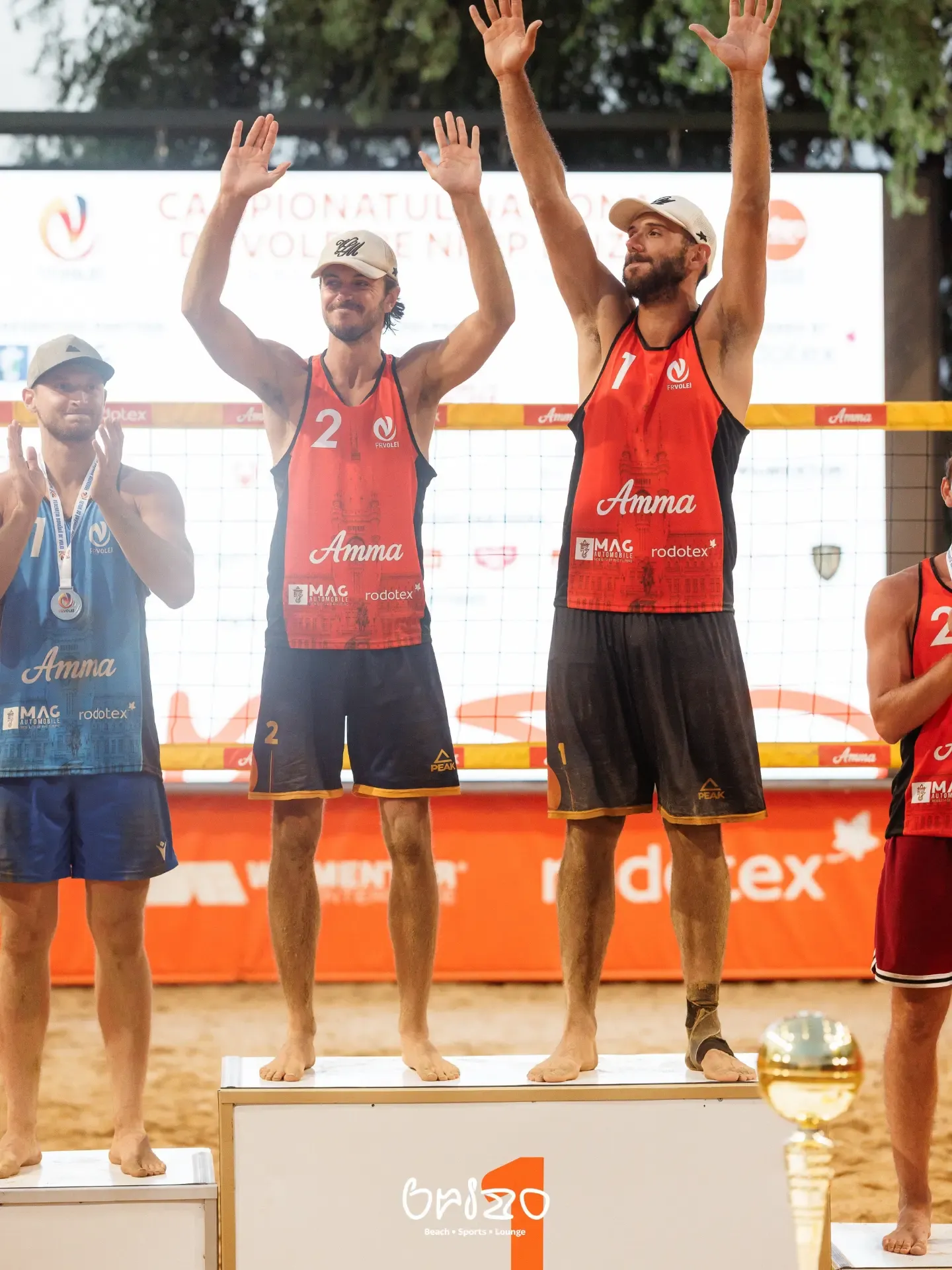 Podiumul de la Campionatul Național de Volei pe Nisip, jucători în tricouri Amma cu brațele ridicate